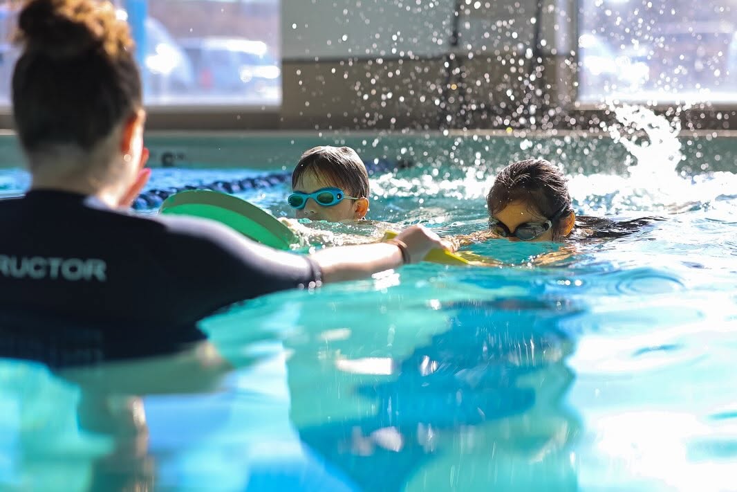 two young swim students swimming toward instructor