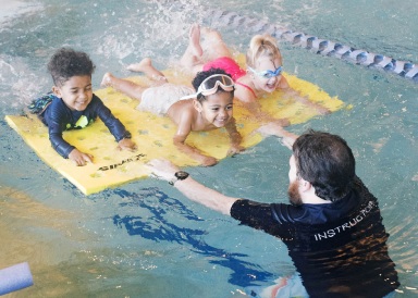 a hudson valley swim teacher teaching three kids how to swim in a swimming pool