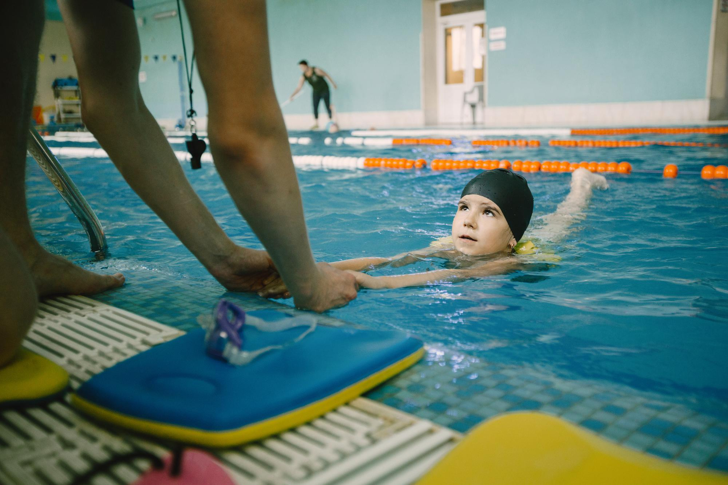child swimming toward instructor in indoor swimming pool